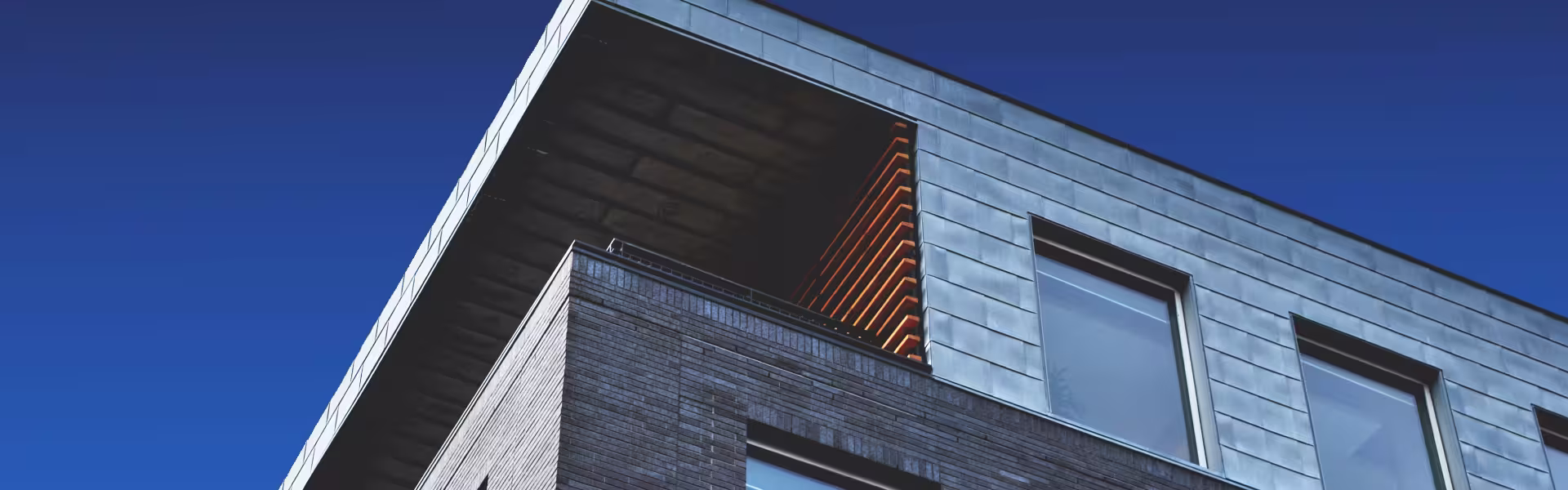 Modern building architecture with brick and metal facade, large windows, and geometric design against clear blue sky