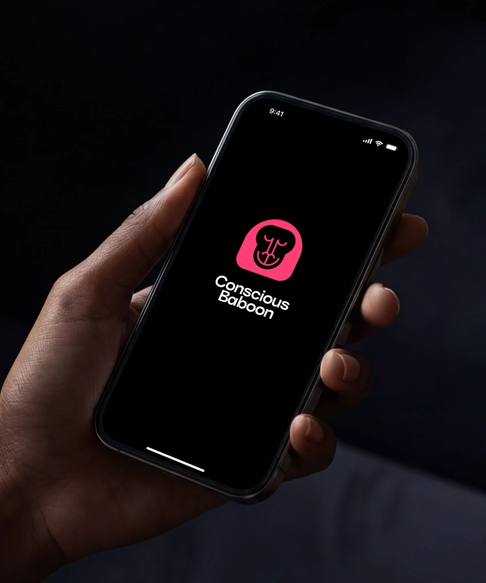 Hand holding a smartphone with the Conscious Baboon logo displayed on a black app loading screen.