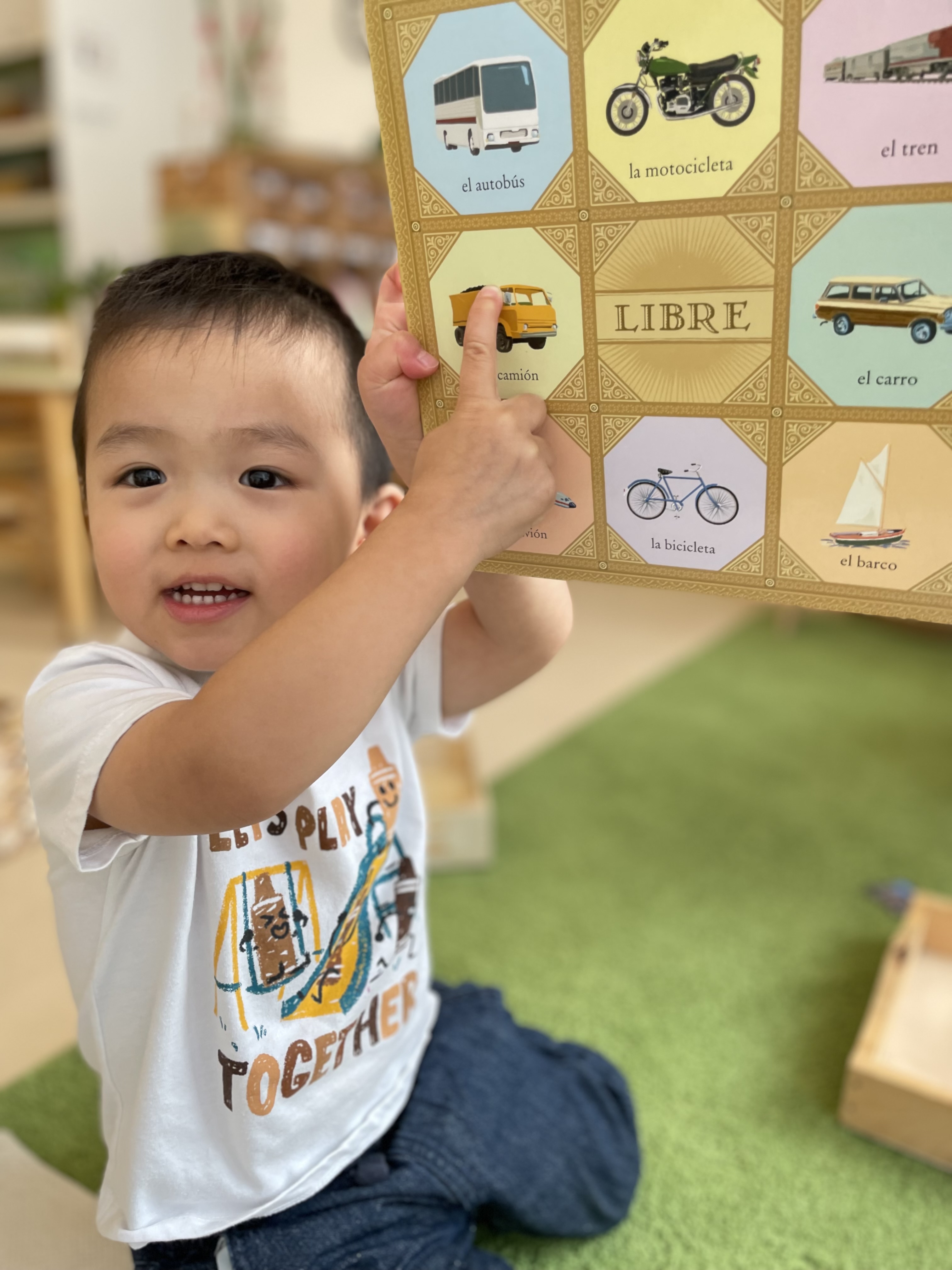 Pine Street School Nursery Student smiling and pointing to his Spanish Language book
