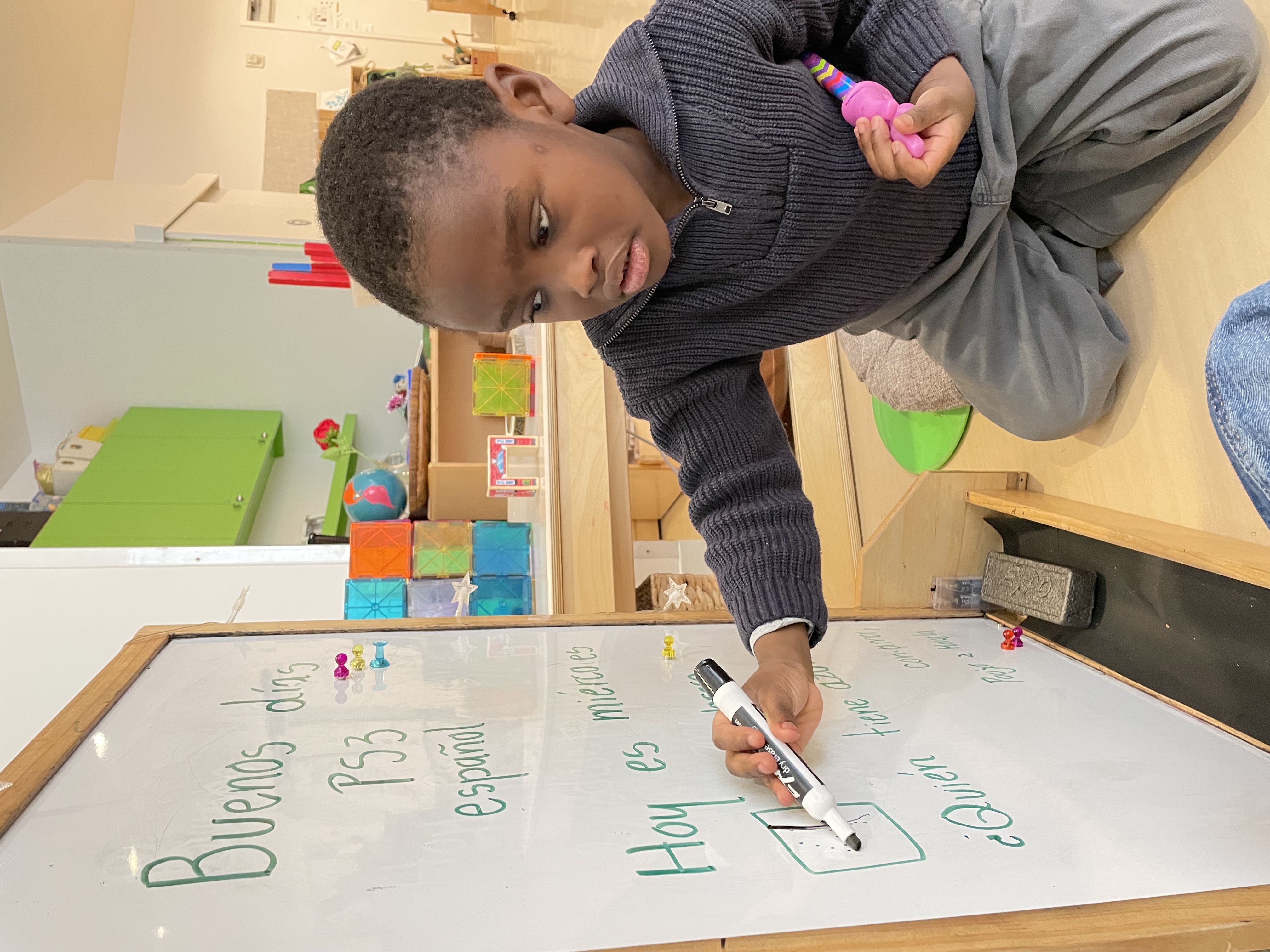 Pine Street School Preschool Spanish Immersion student writes on a whiteboard in the classroom.
