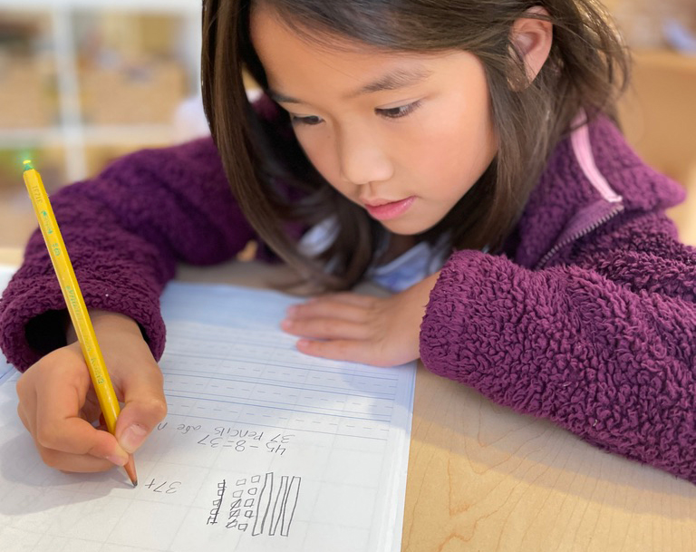 Pine Street School elementary student focused on solving a math equation in her notebook.