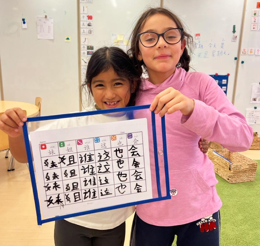 Two Pine Street School Elementary students holding up their Mandarin writing, building confidence in written communication and language learning.