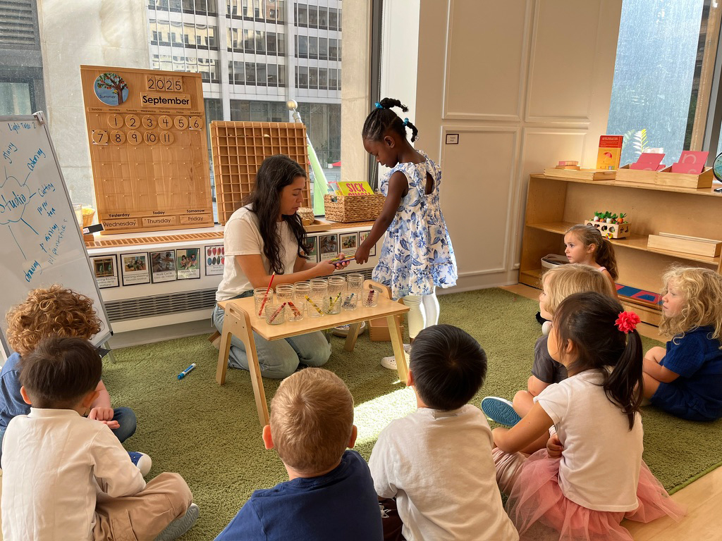 A Junior Kindergarten classroom moment - students are seated in a circle while one student is engaging with the teacher.
