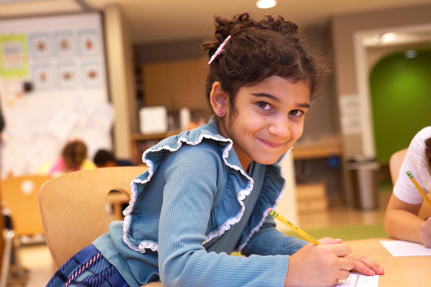 Elementary student smiles while writing at her desk in the classroom.