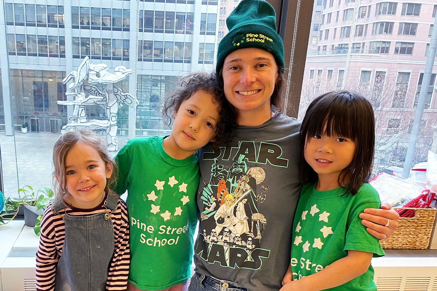 Pine Street School Kindergarten teacher posing with three students in front of classroom window over looking Fosun plaza in Financial District.