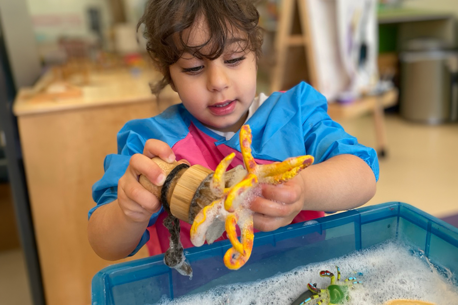 Pine Street School Nursery student washing toys at a water table during a Montessori Practical Life activity, building independence, coordination, and concentration.
