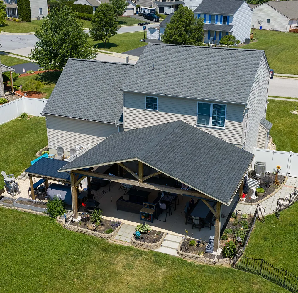 Aerial view of a suburban house with a large covered patio, outdoor furniture, with a brand new shingle roof.