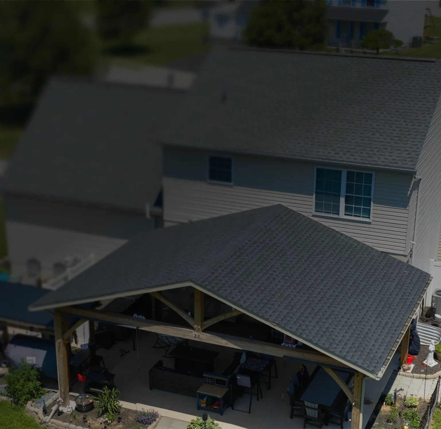 Aerial view of a two-story house with a dark gray shingled roof, featuring an attached patio cover.