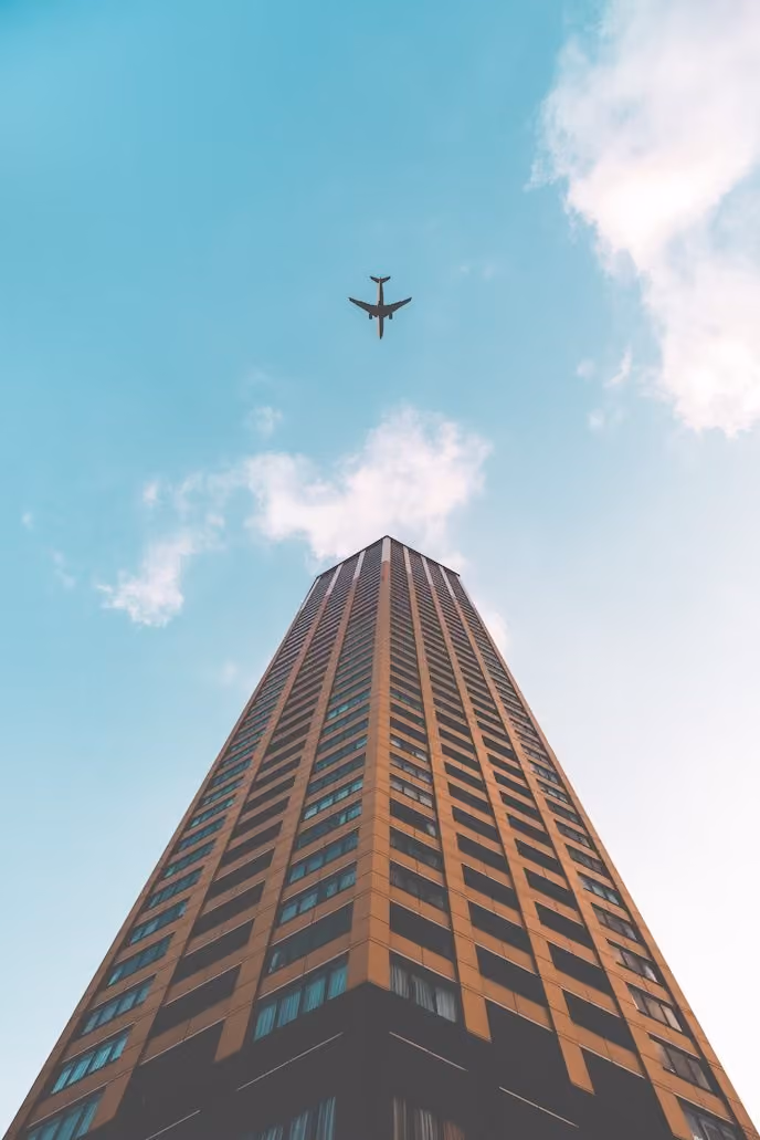 Airplane flying over the top of a tall building against a partly cloudy blue sky.