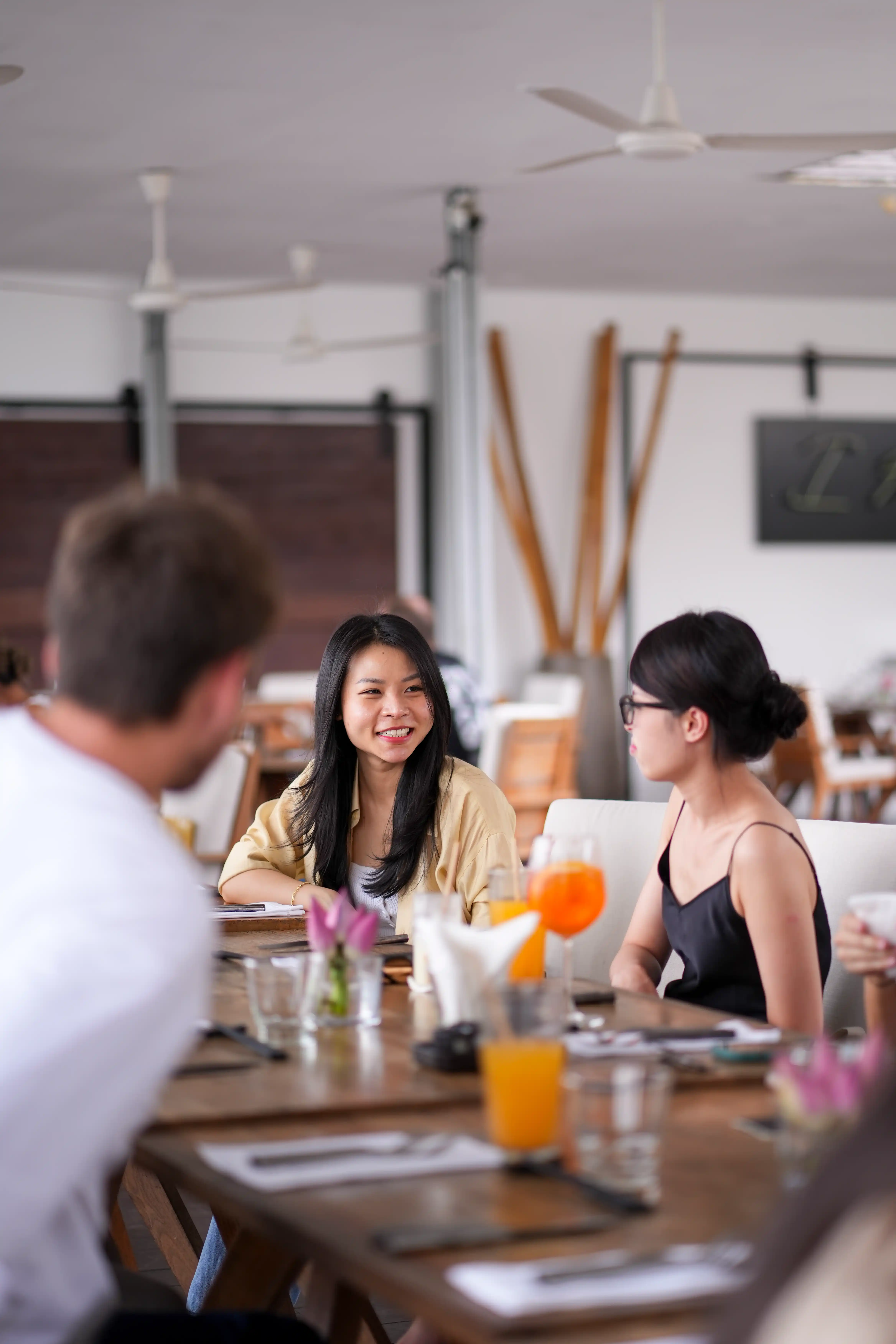 Young people sitting around a table in a cafe, chatting and smiling with drinks on the table.