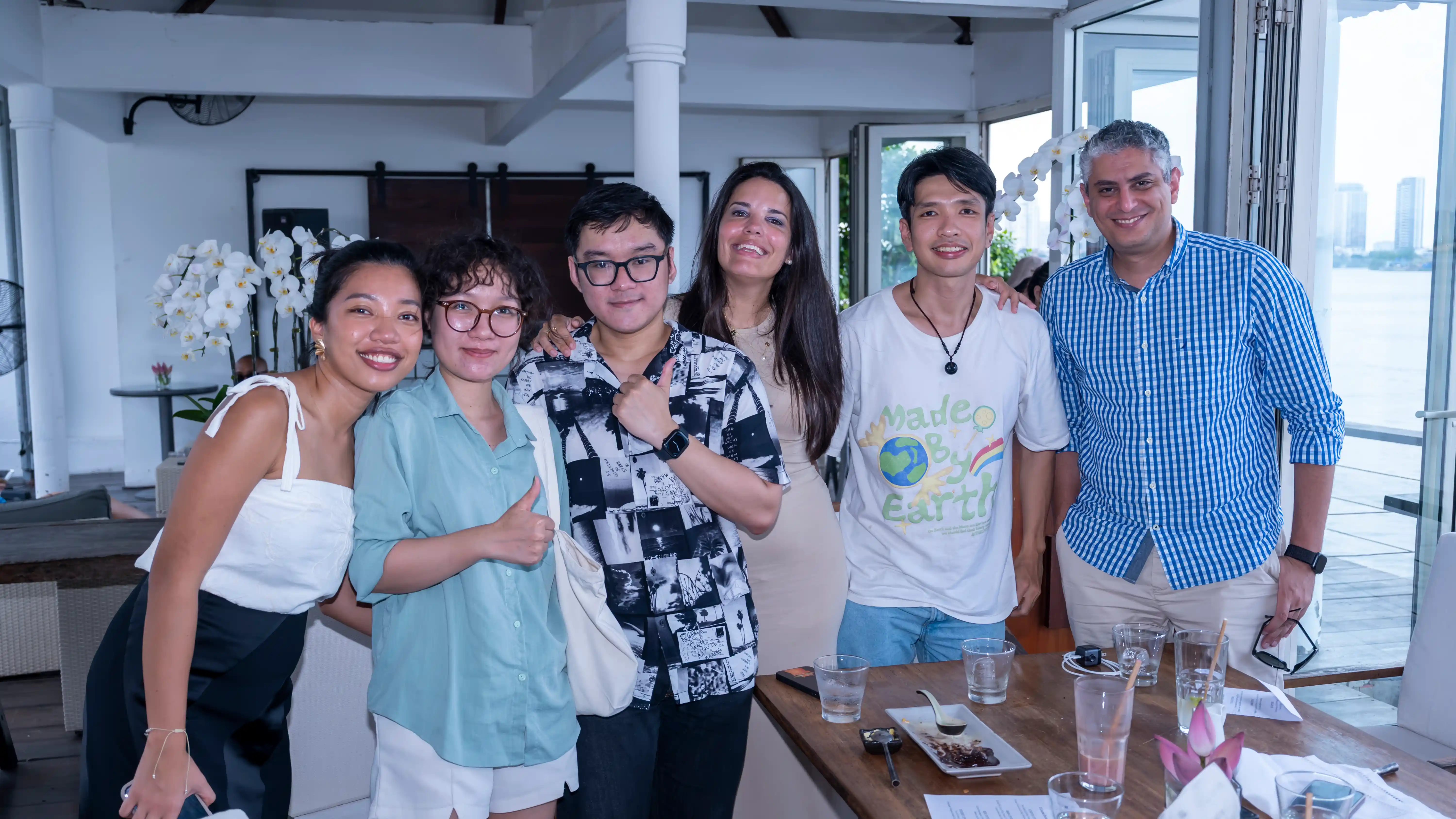 Group of six diverse young adults smiling indoors near a table with drinks and food.