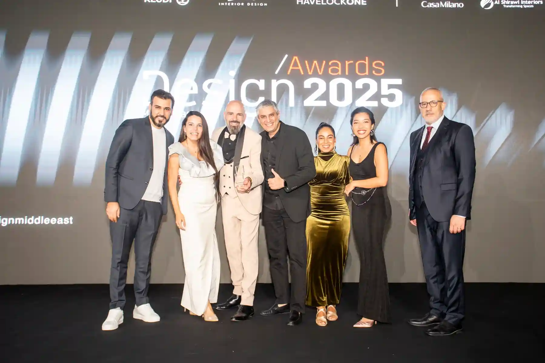 Group of six people dressed formally posing on stage at Design Awards 2025 event.