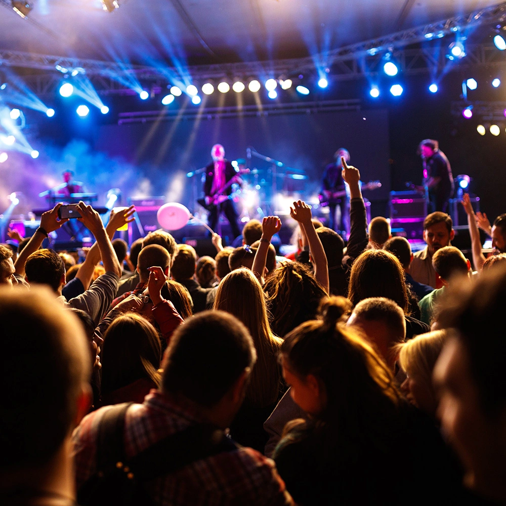 Publikum feiert auf einem Konzert mit einer Band, die auf einer Bühne unter bunten Lichtern spielt.