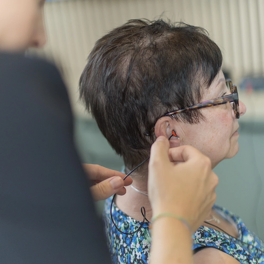 Frau bekommt ein kleines Hörgerät ins rechte Ohr eingesetzt, gesehen von der Seite.