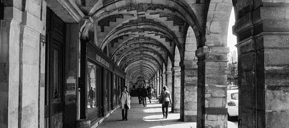 Passage voûté en pierre avec des personnes marchant et des voitures visibles au loin.