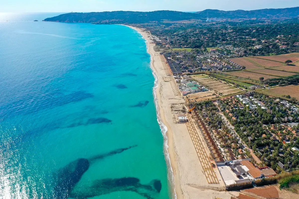 Vue aérienne de la plage de Pampelonne, avec ses eaux turquoise, son long ruban de sable bordé de clubs de plage et de villas verdoyantes.