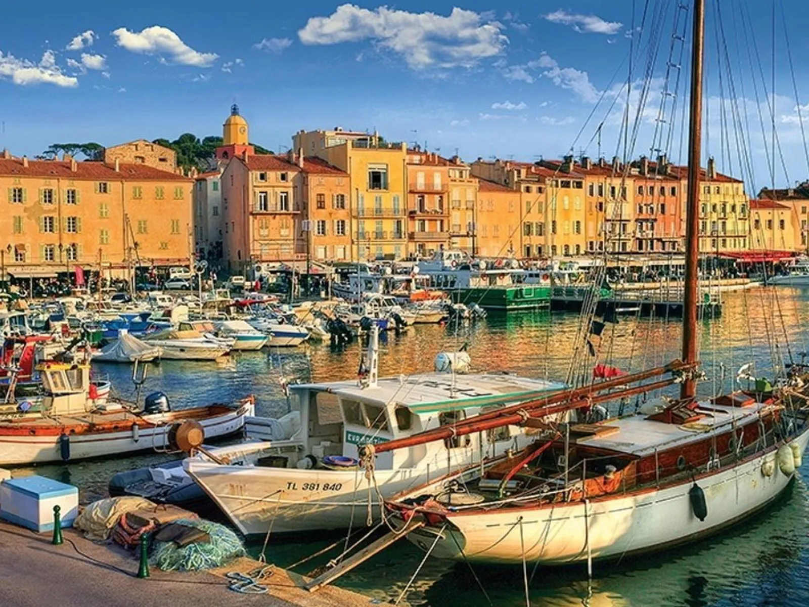 Port pittoresque de Saint-Tropez au coucher de soleil, avec bateaux de pêche et voiliers amarrés devant les façades colorées et le clocher de l'église.