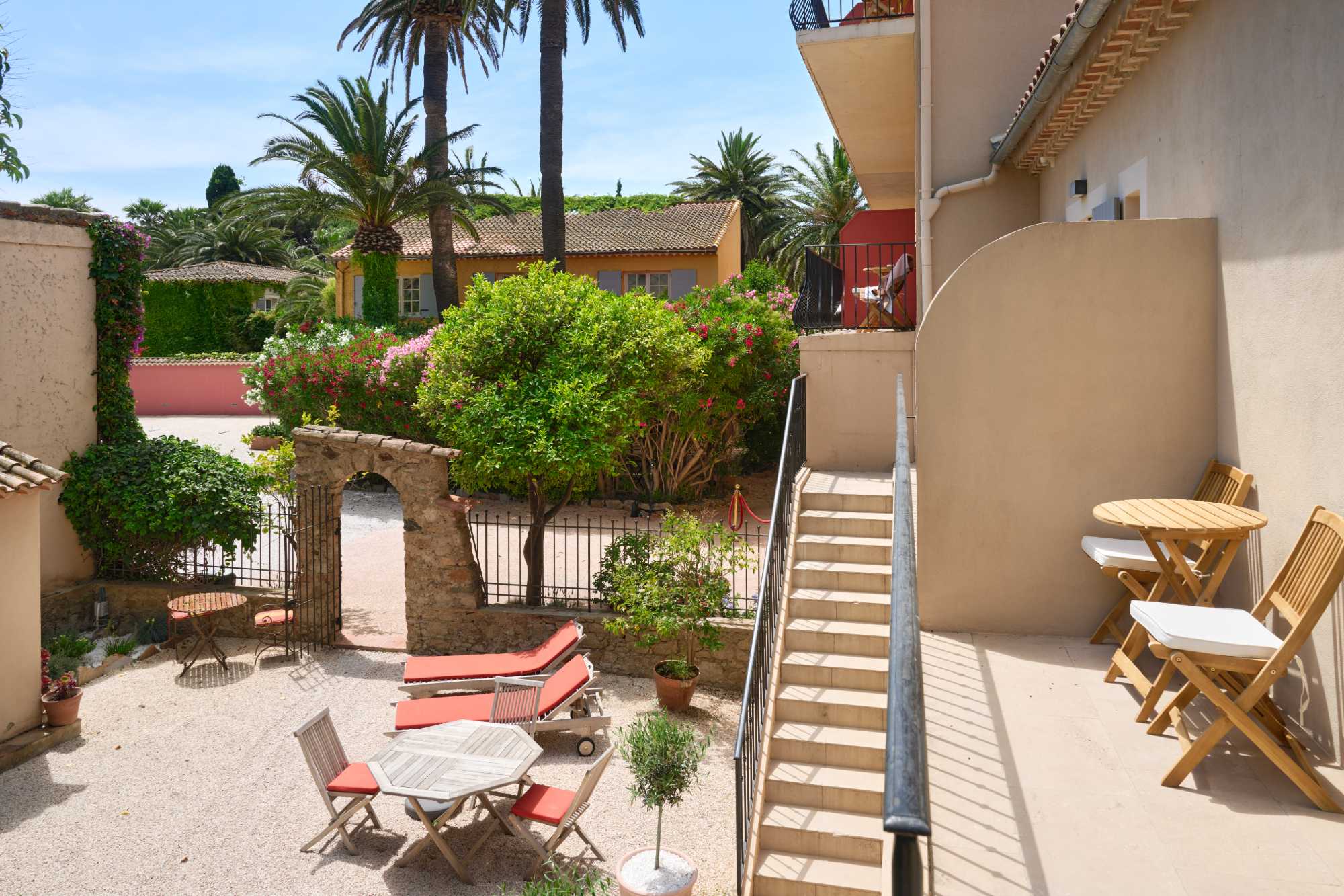 Terrasse en étages d'une propriété méditerranéenne, avec escalier extérieur, mobilier de jardin, arche en pierre et jardin luxuriant planté de palmiers et de bougainvillées.