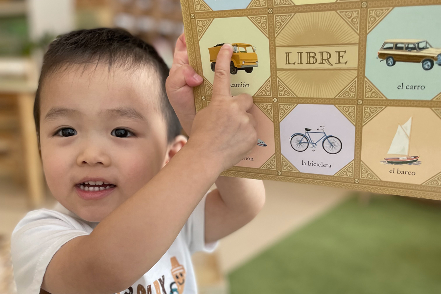 Pine Street School Nursery Student smiling and pointing to his Spanish Language book