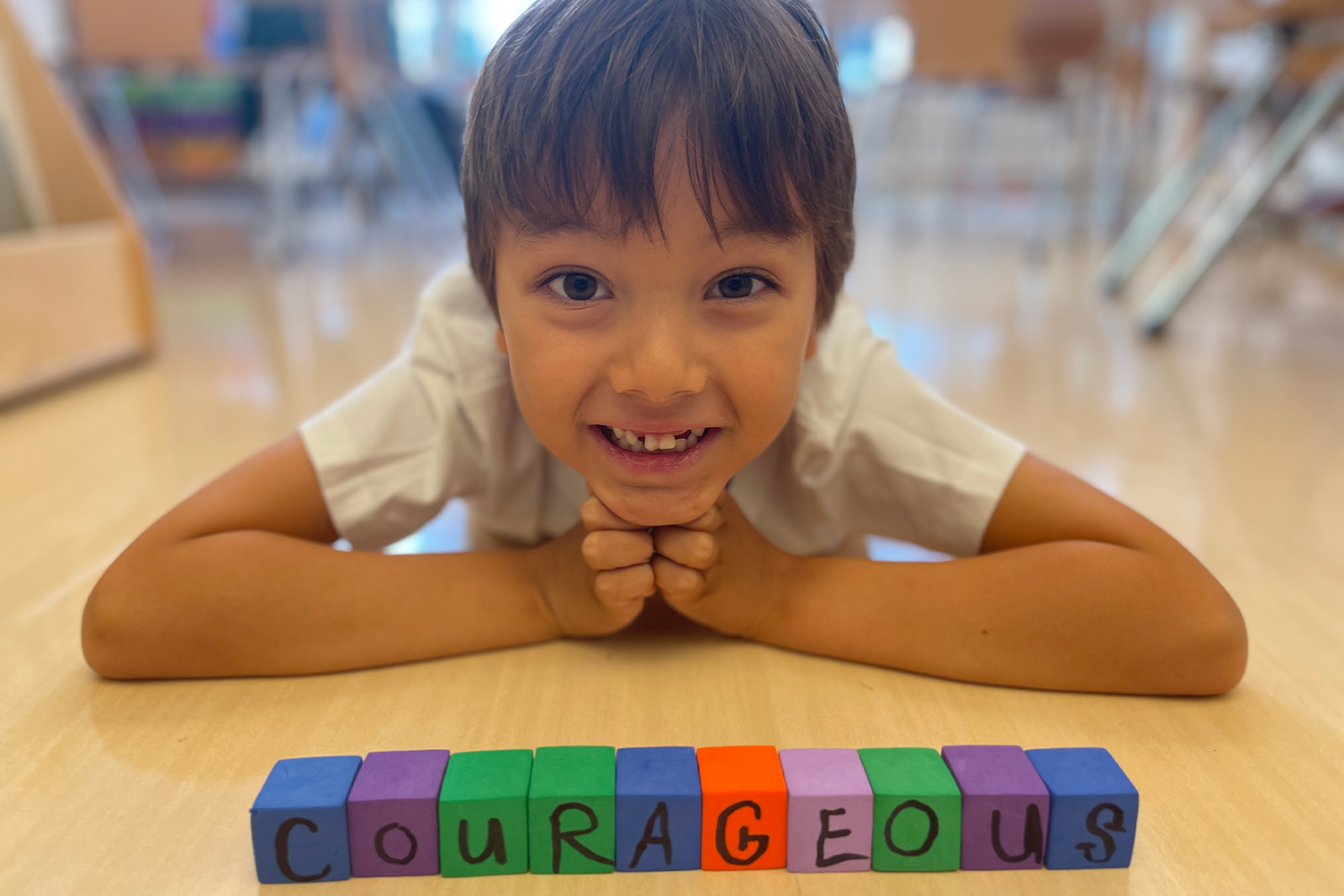 Student smiling with his letter blocks that spell "Courageous"