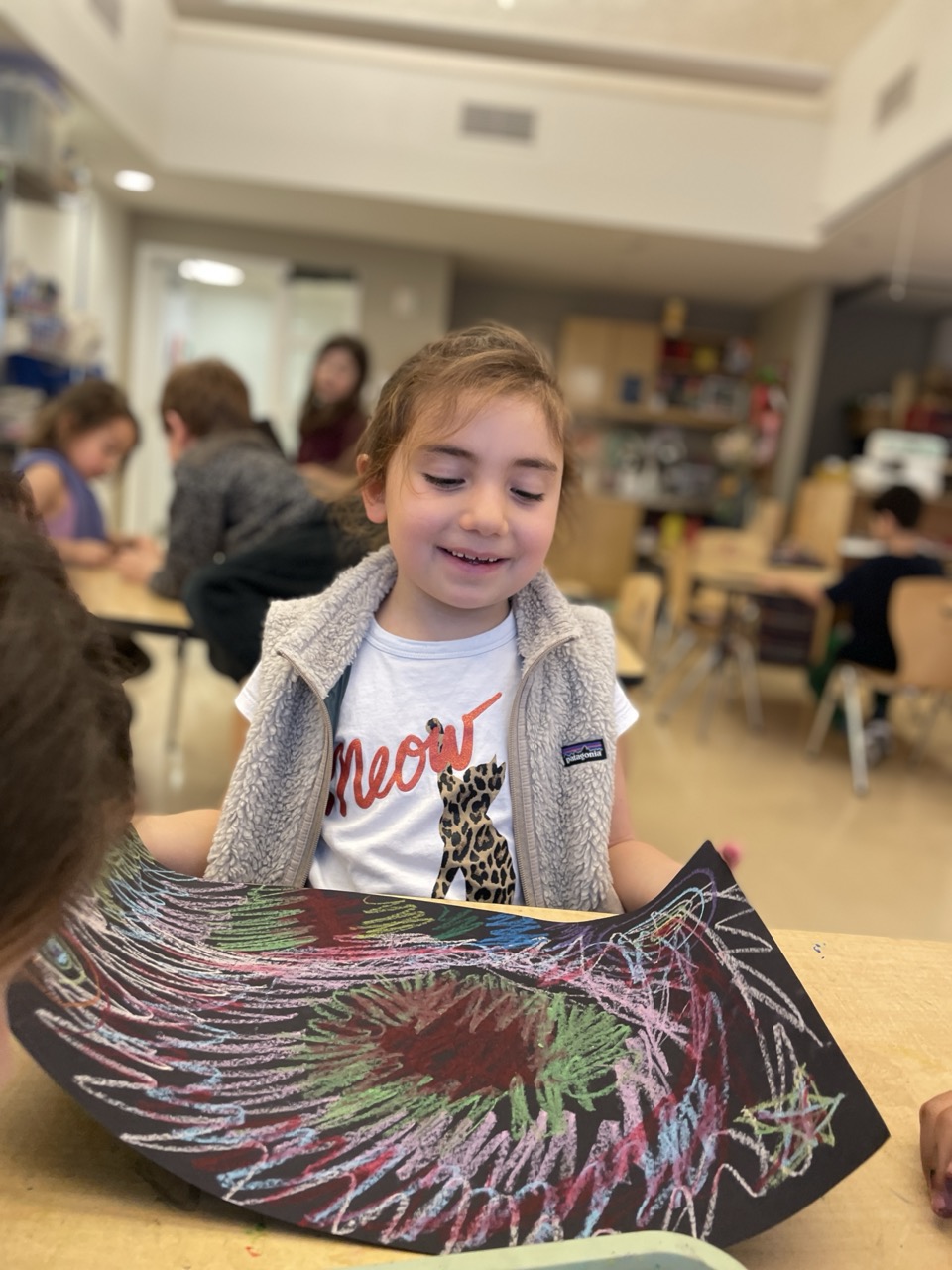 Student smiles in front of her art piece in the classroom