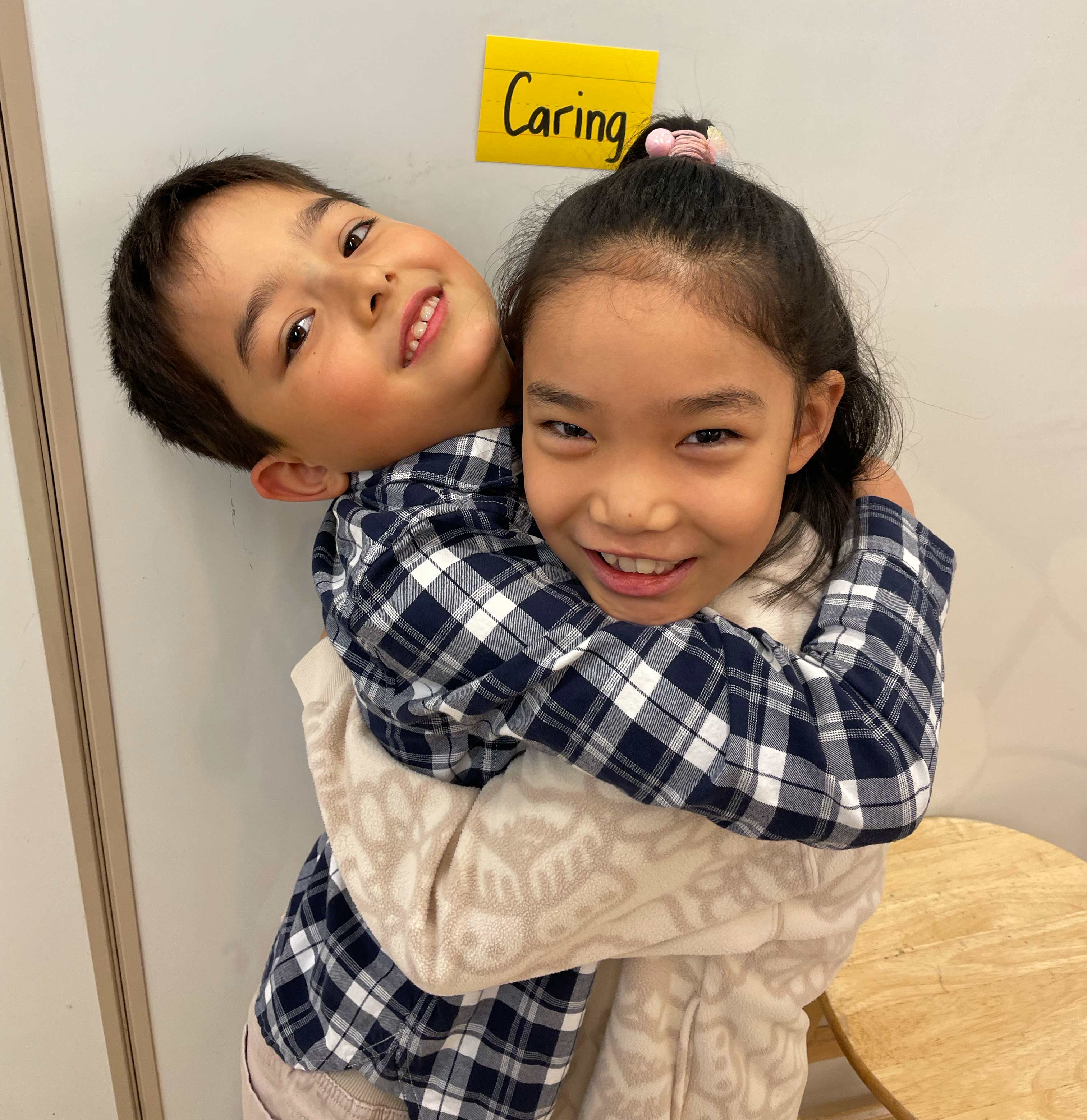 Friends hugging in front of a post it note that says "Caring"