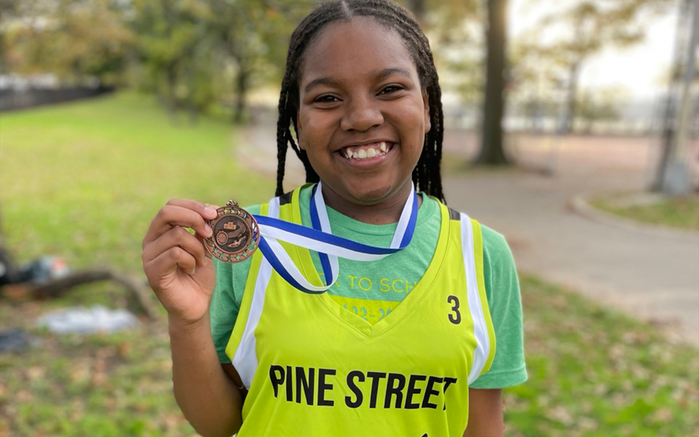Cross Country team member holds up her medal and smiles