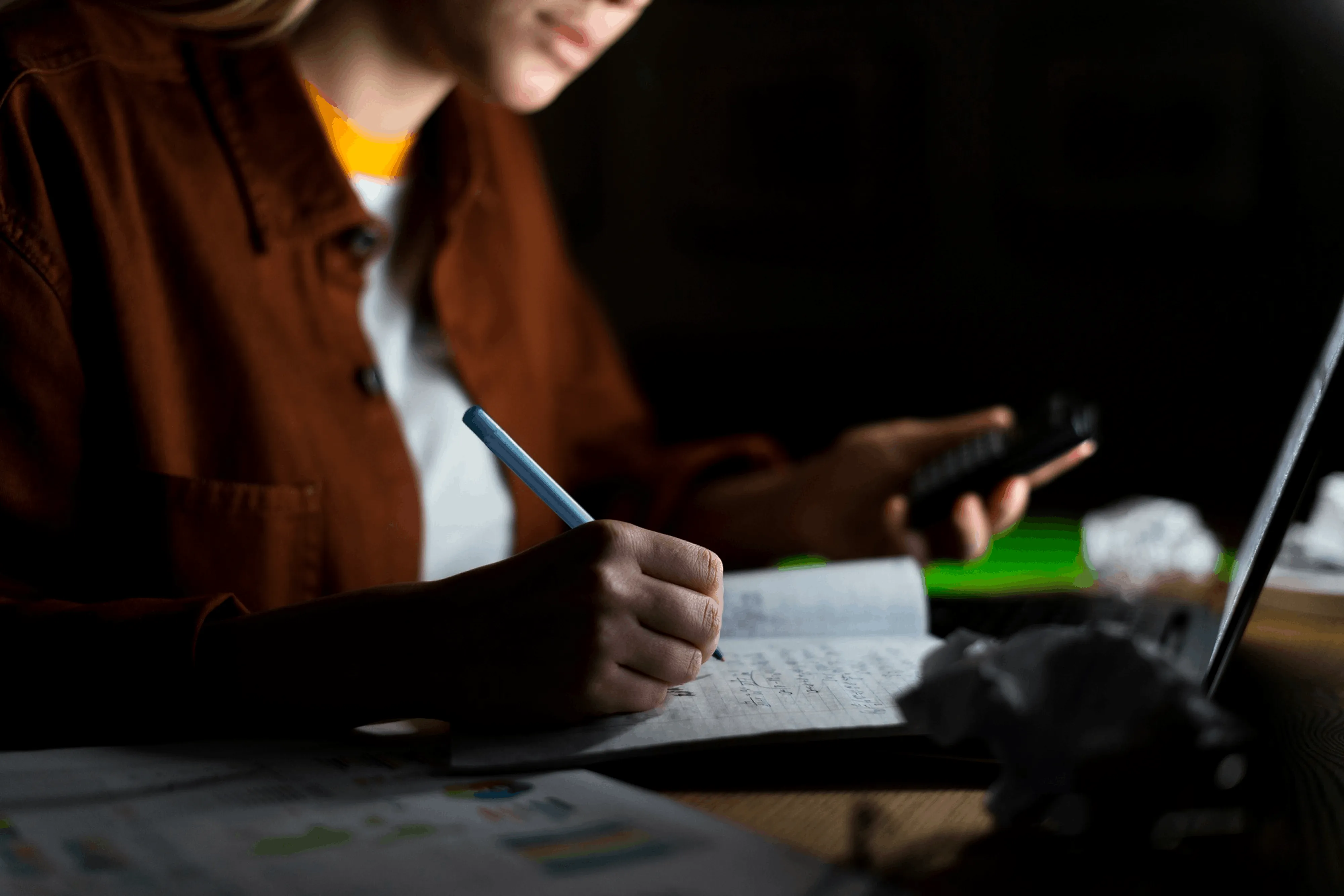 Business professional taking notes while reviewing information on a laptop and smartphone