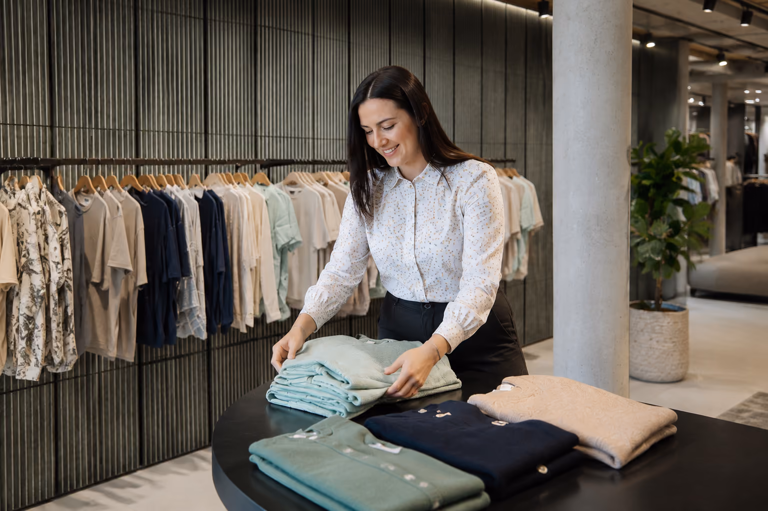 Person legt Pullover auf einem Tisch in der Modeabteilung zusammen