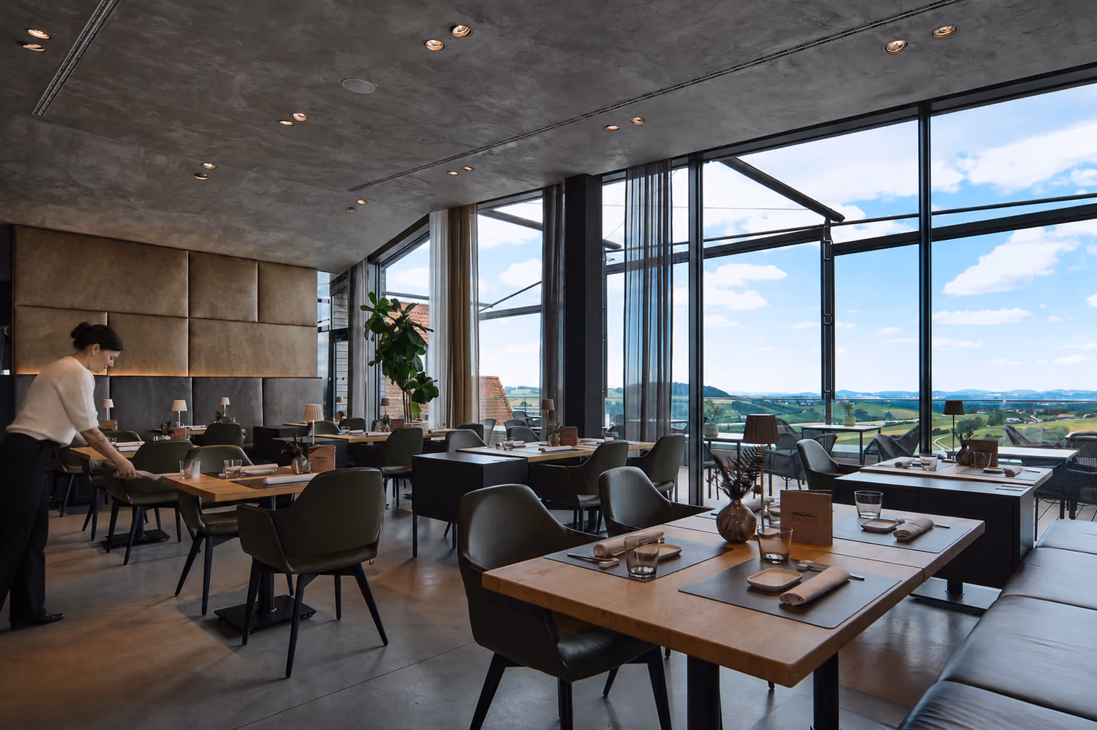 Gastraum des Restaurants JOHANNS mit Panoramafenstern, eine Servicekraft deckt einen Tisch ein