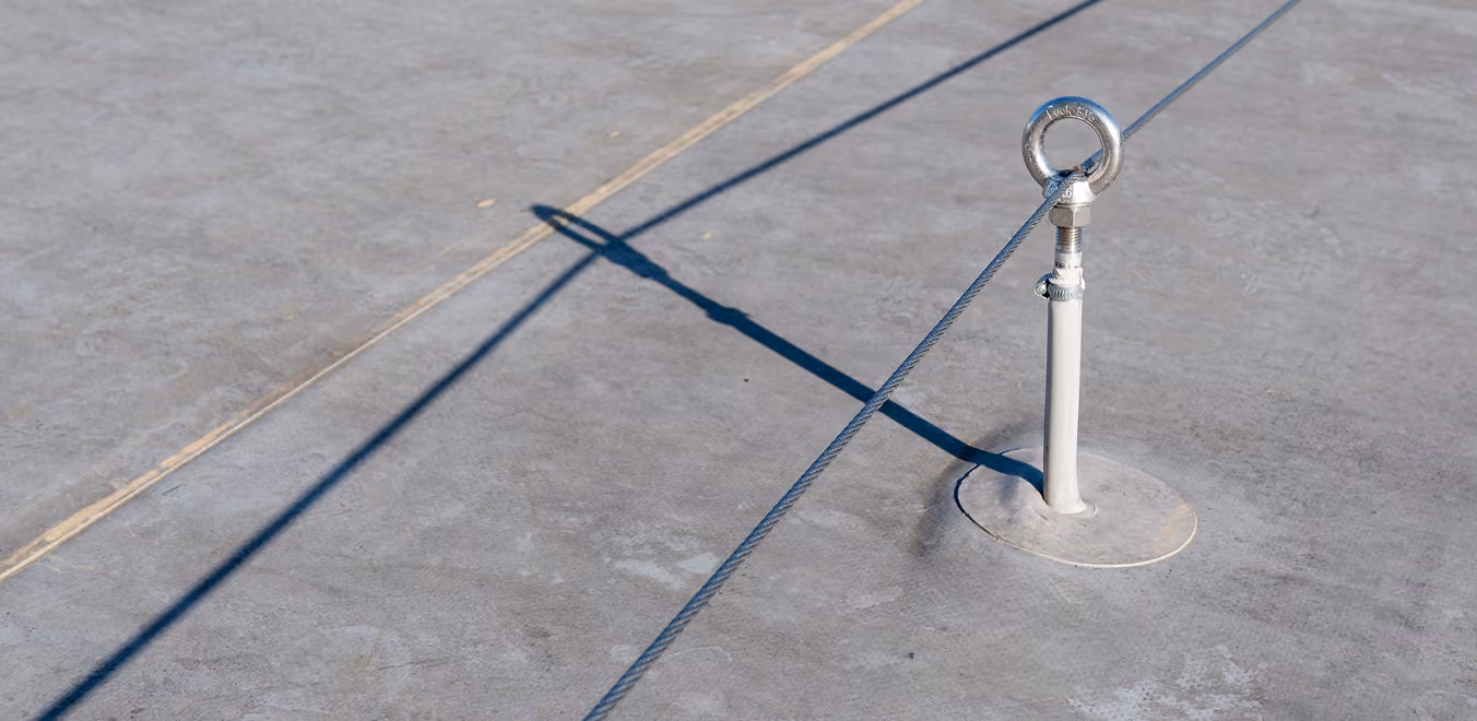 Metallöse mit gespanntem Drahtseil auf grauer Betonoberfläche mit Schatten.