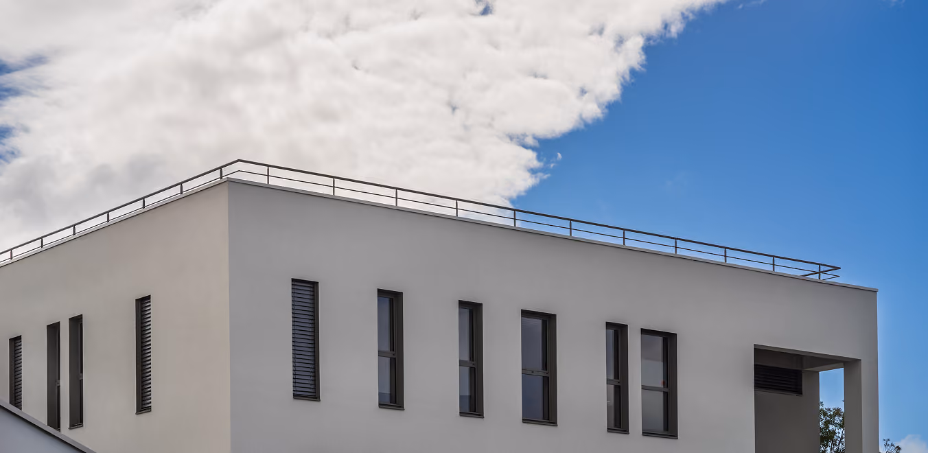Modernes graues Gebäude mit schmalen Fenstern unter einem bewölkten blauen Himmel.