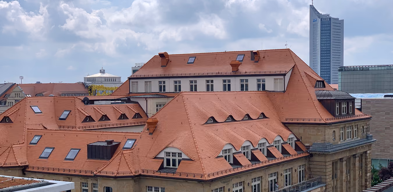 Blick auf Gebäude mit roten Ziegeldächern und im Hintergrund moderner Wolkenkratzer.