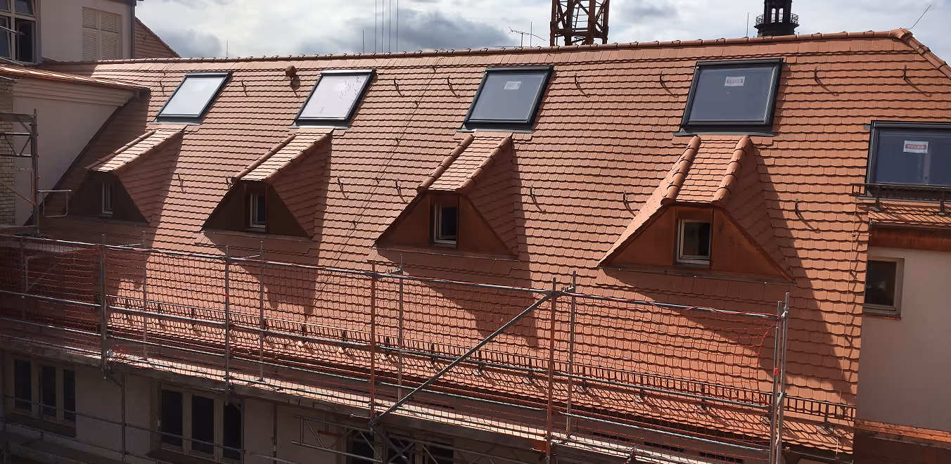 Dach mit roten Ziegeln, vier Gaubenfenstern und fünf Dachfenstern, eingerüstet für Bauarbeiten.