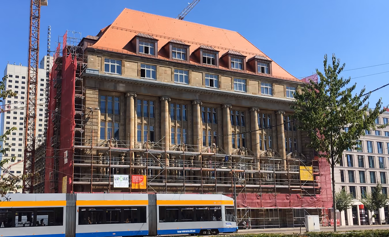 Historisches Gebäude mit Säulen und Gerüst, davor fährt eine Straßenbahn bei klarem Himmel.