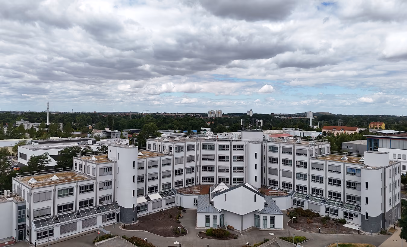 Modernes weißes Bürogebäude mit vielen Fenstern und bewölktem Himmel im Hintergrund.
