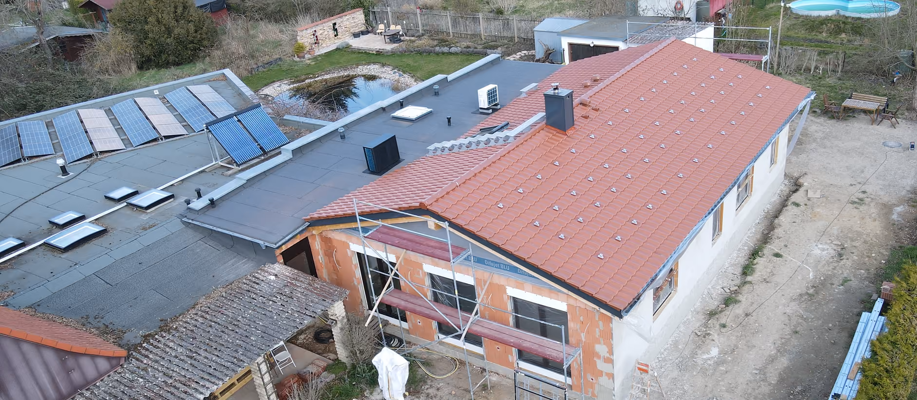 Neubau eines Hauses mit Dachziegeln, Solarpaneelen und Baustellengerüst in ländlicher Umgebung.
