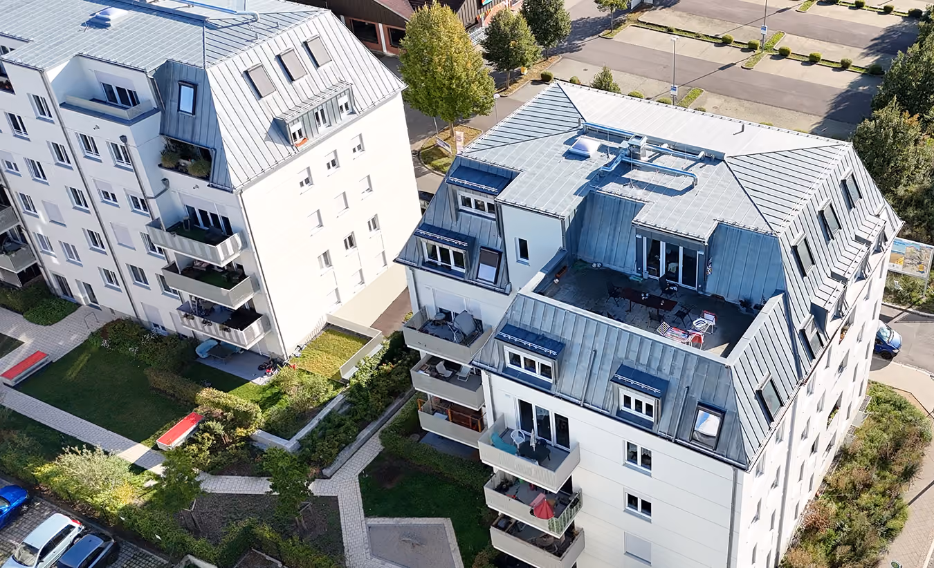 Luftaufnahme von zwei modernen weißen Wohngebäuden mit Balkonen, Dachterrassen und Grünflächen.