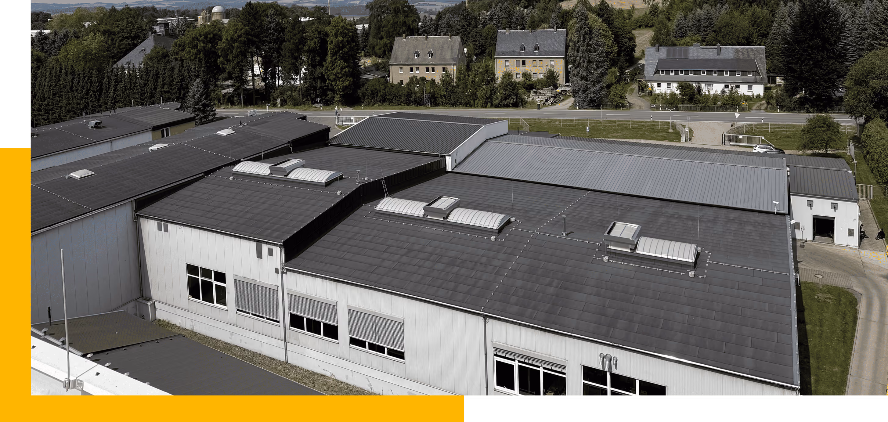 Industriegebäude mit grauen Dächern und geöffneten Jalousien in einem grünen Vorortsgebiet.