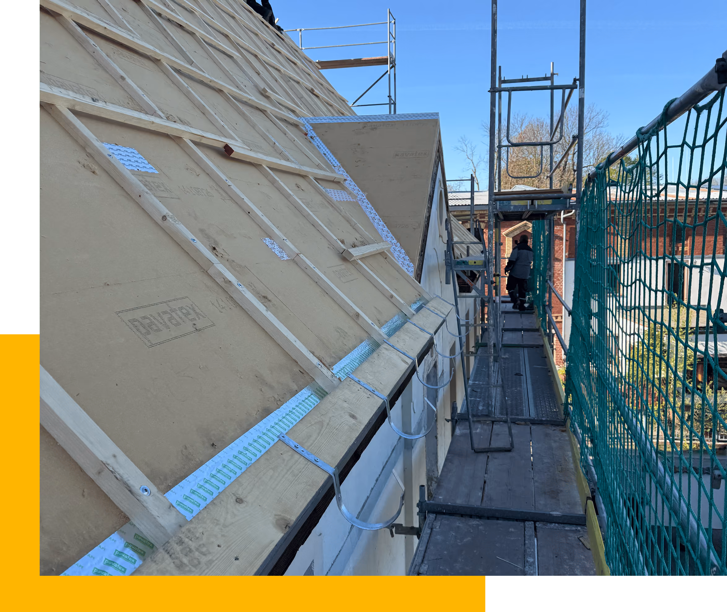 Dachbau mit Latten auf einer Unterlage und Gerüst mit Arbeiter bei sonnigem Himmel.