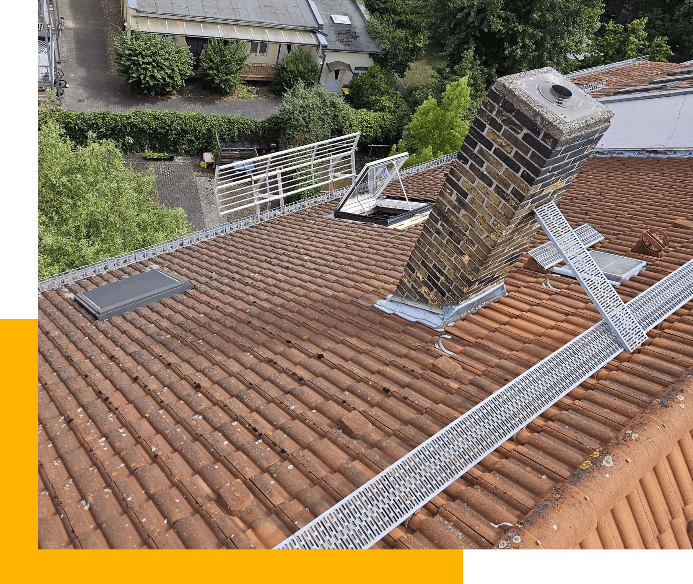 Ziegeldach mit offenem Dachfenster, Schornstein und umlaufendem weißem Regenrinnenschutz.