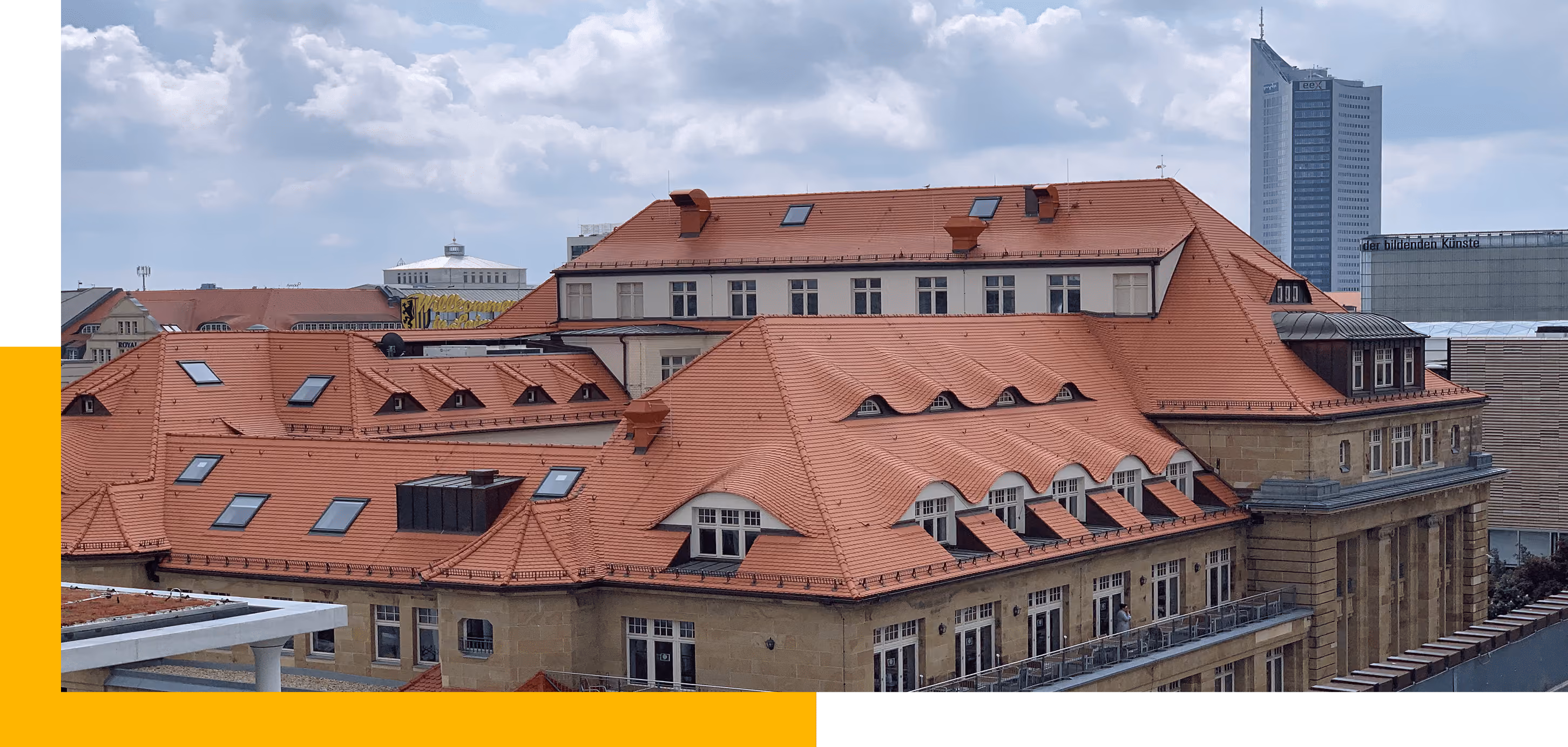 Rotes Ziegeldach auf einem historischen Gebäude mit moderner Stadtansicht und bewölktem Himmel.