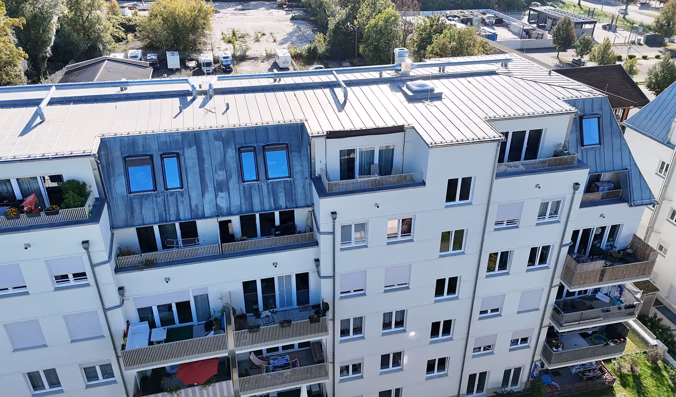 Vogelperspektive eines modernen Wohngebäudes mit Balkonen und bepflanzten Terrassen.