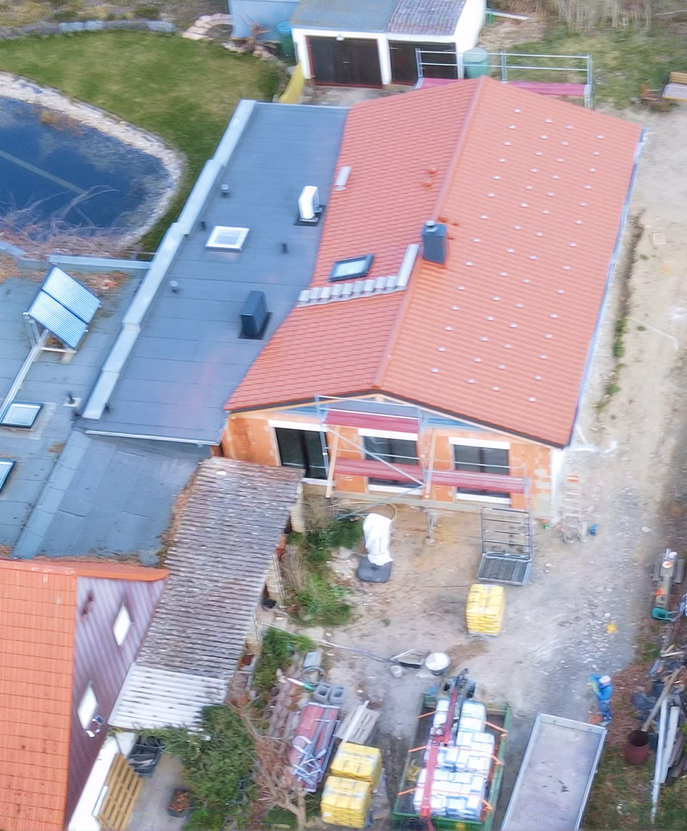 Vogelperspektive eines Wohnhauses im Bau mit rotem Dach und Baustoffen im Hof.