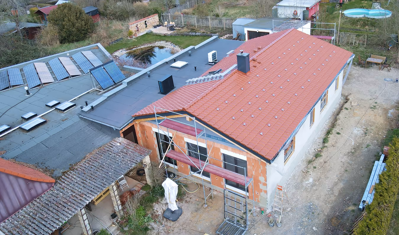 Luftaufnahme eines Hauses im Bau mit roten Dachziegeln, Gerüst und umliegendem Garten.