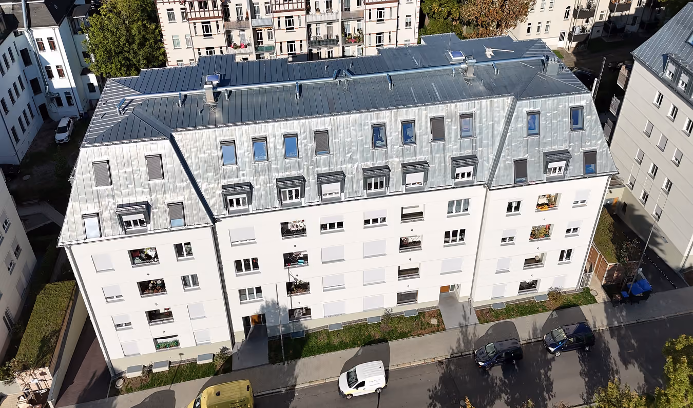 Luftaufnahme eines mehrstöckigen Wohngebäudes mit Metallfassade und geparkten Autos davor.