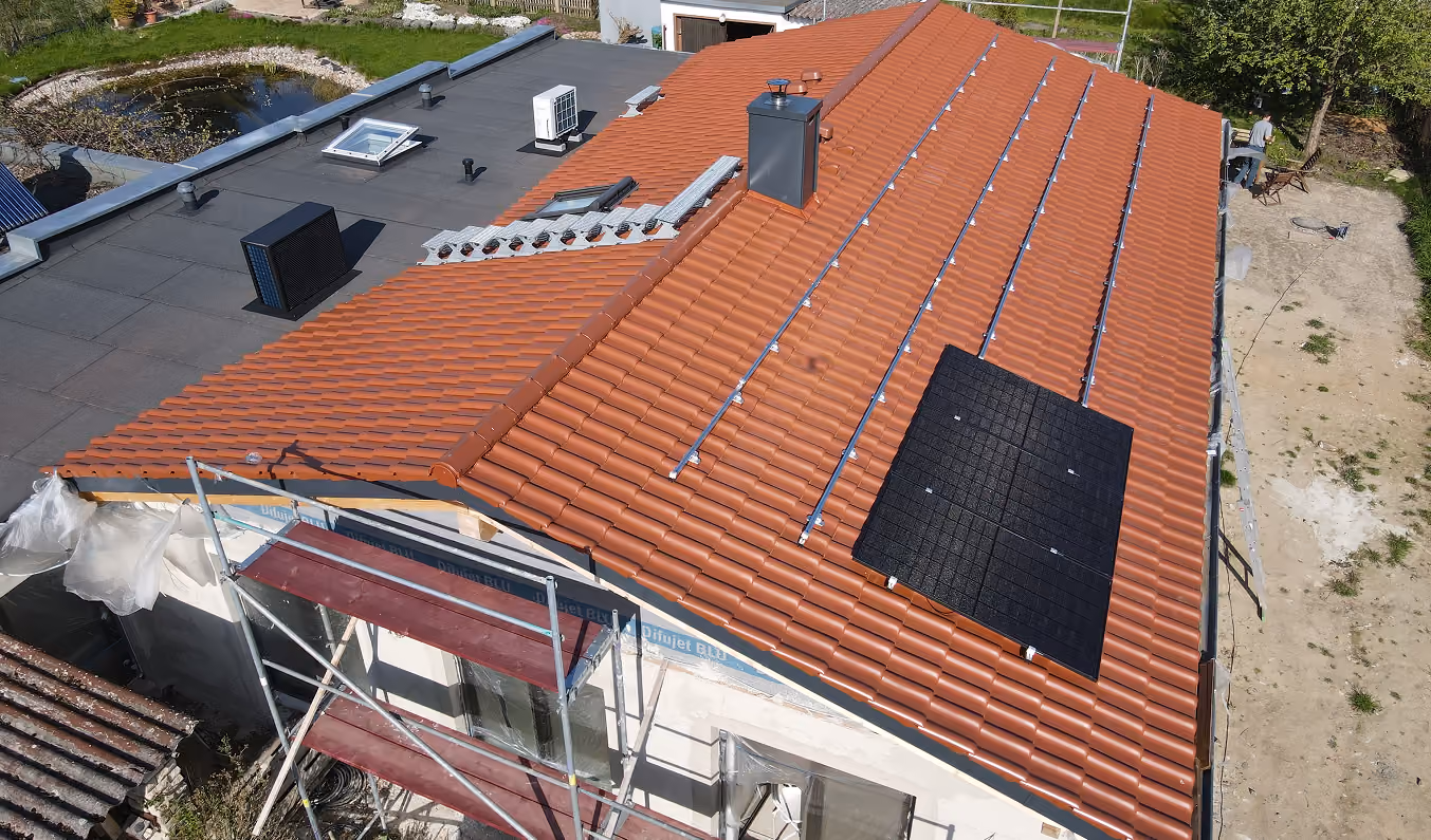 Hausdach mit roten Ziegeln, teilweise installierten Solarpanelen und Gerüst auf der Vorderseite.