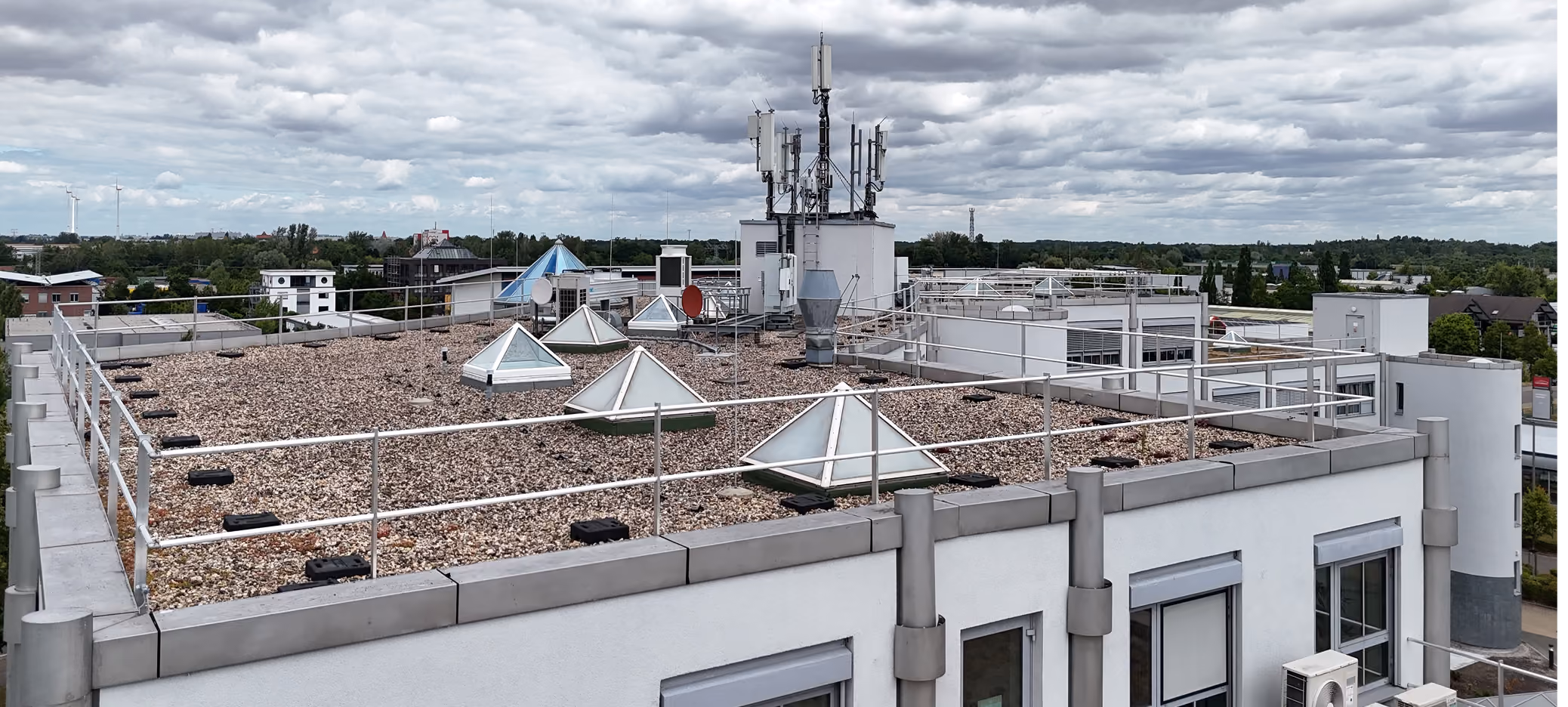 Flachdach mit Glaspyramiden und Antennen unter bewölktem Himmel in einer städtischen Umgebung.