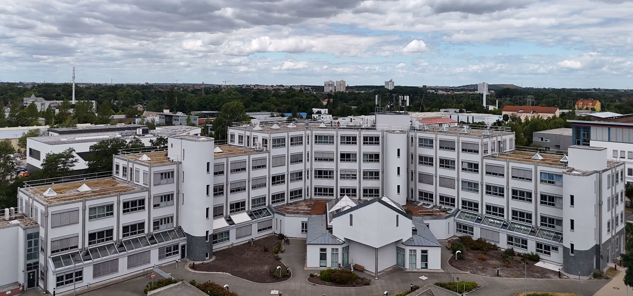 Großes weißes Büro- oder Verwaltungsgebäude mit vielen Fenstern unter bewölktem Himmel.
