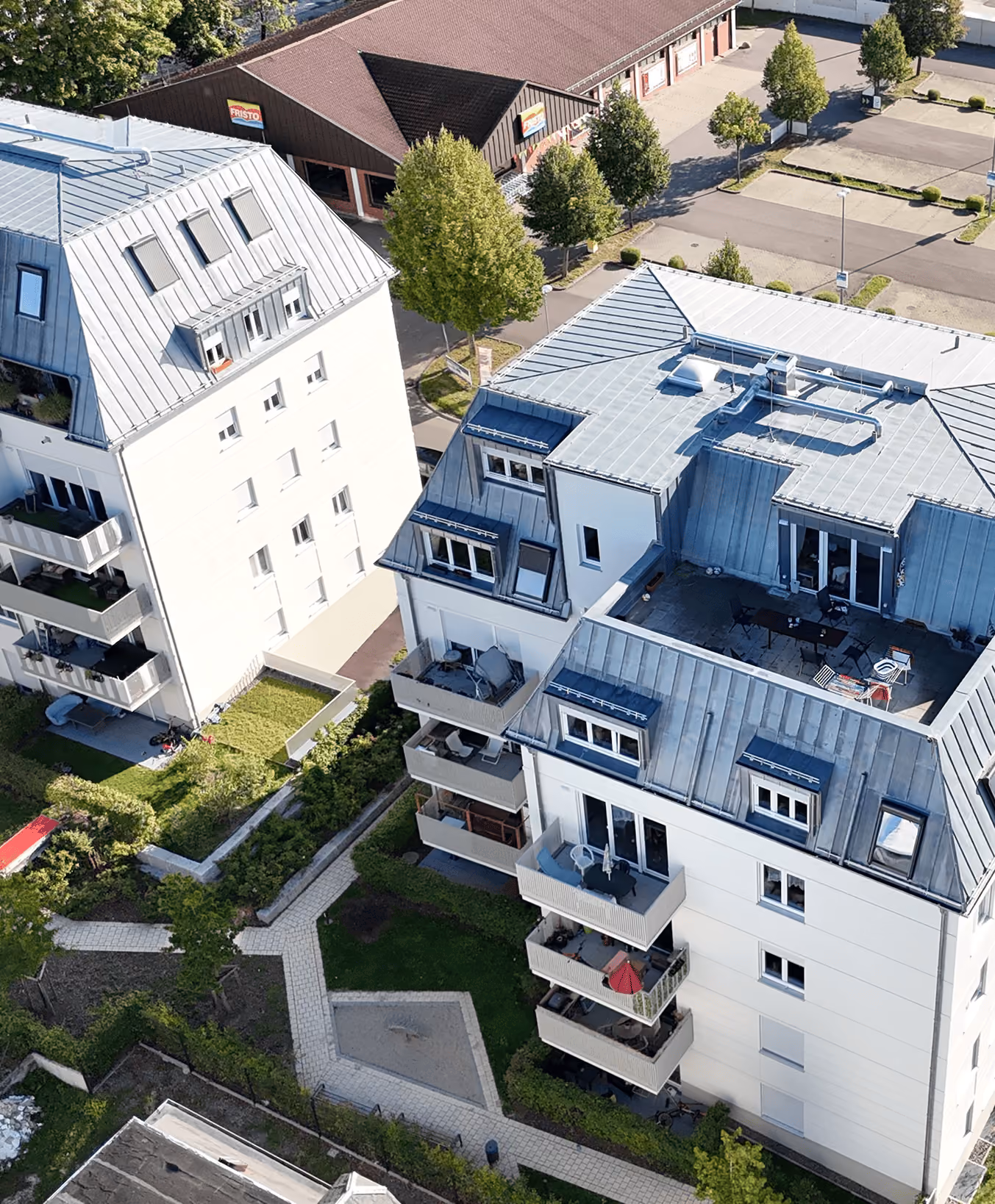 Luftaufnahme von zwei weißen Wohngebäuden mit Balkonen, Bäumen und Gehwegen dazwischen.